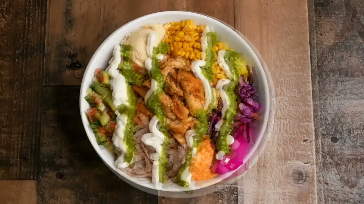 A finished bowl with zig-zags of white garlic toum and green zhug