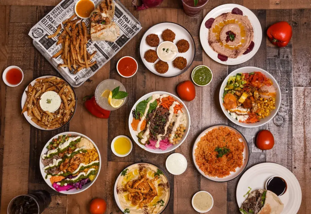 A wood table spread with bowls, fries, falafel, hummus and dips for a group